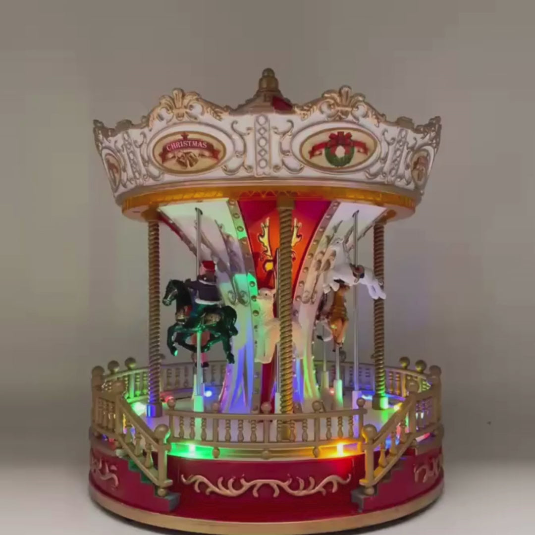 Video della giostra natalizia decorata nei toni del rosso e dell’oro con cavalli in movimento e luci LED multicolore alla base.