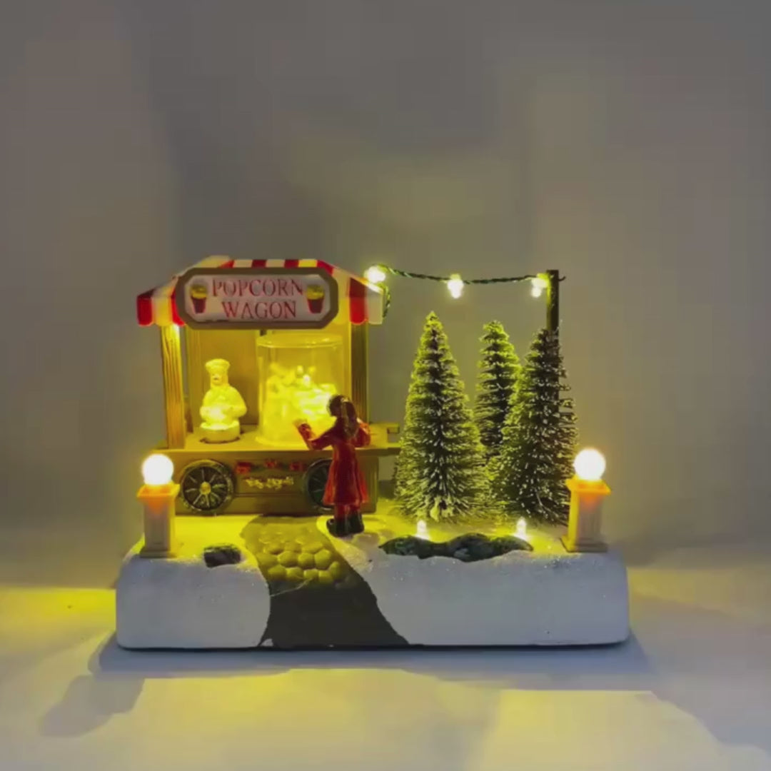 Video con musica natalizia Miniatura natalizia della bancarella Popcorn Wagon con personaggio in cappotto rosso e alberi innevati decorativi.