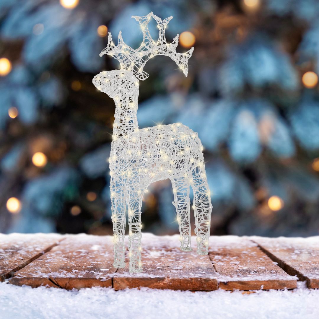 Figura natalizia a forma di renna alta 110cm illuminata con micro LED, posizionata su tavola innevata con sfondo natalizio.