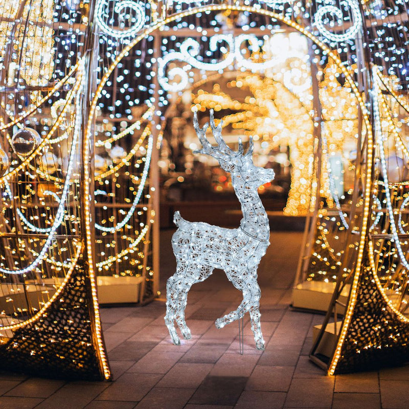 Renna natalizia luminosa alta 125 cm accesa con LED bianco freddo, collocata in un’ambientazione notturna ricca di decorazioni e luci natalizie.