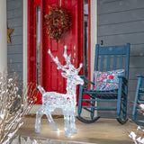 Renna luminosa 65 cm in acrilico con LED bianchi posizionata all’esterno davanti a una porta rossa decorata per Natale.