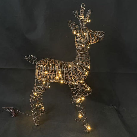 Decorazione natalizia a forma di renna con una zampa anteriore alzata in rattan illuminata da luci LED bianco caldo su sfondo scuro.