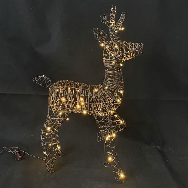 Decorazione natalizia a forma di renna con una zampa anteriore alzata in rattan illuminata da luci LED bianco caldo su sfondo scuro.