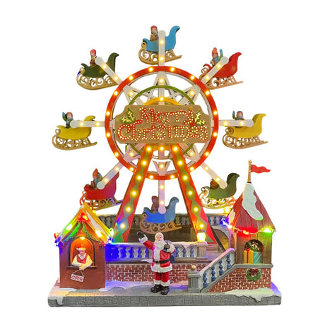 Ruota panoramica natalizia illuminata con slitte colorate, insegna Merry Christmas al centro e Babbo Natale in piedi davanti alla giostra.
