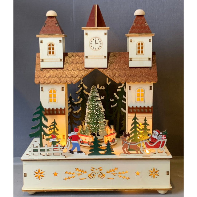 Scena natalizia in legno illuminata con albero rotante, Babbo Natale sulla slitta, pattinatori e casetta con torre e orologio decorata con luci calde.