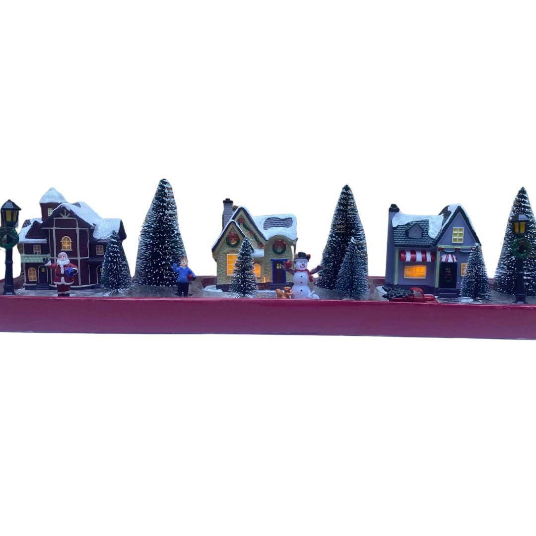 Set natalizio in miniatura con case illuminate, alberi innevati, Babbo Natale, pupazzo di neve e personaggi su confezione rossa.