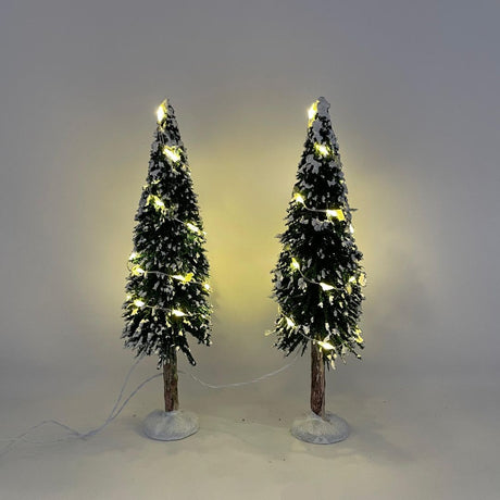 Due alberi natalizi decorativi con neve artificiale e micro LED caldi accesi, su base bianca.
