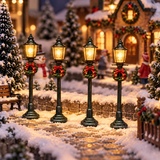 Set di 4 lampioni natalizi illuminati disposti lungo un vialetto innevato di un villaggio di Natale, con case decorate, abeti e personaggi sullo sfondo