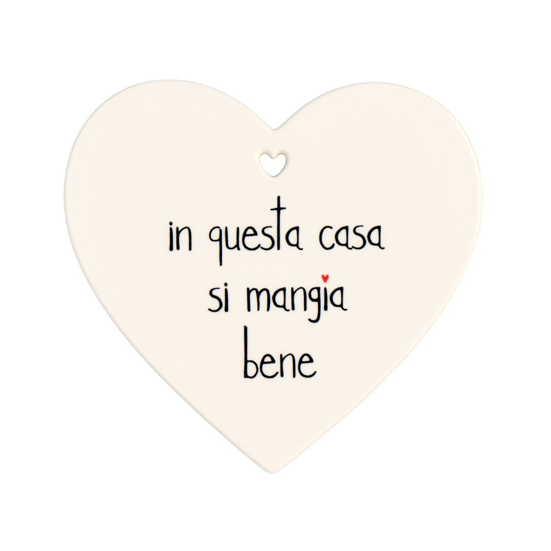 Sottopentola a forma di cuore in grès con scritta nera "in questa casa si mangia bene".