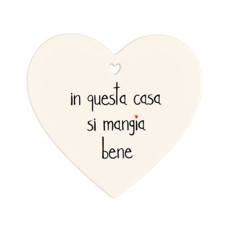 Sottopentola a forma di cuore in grès con scritta nera "in questa casa si mangia bene".