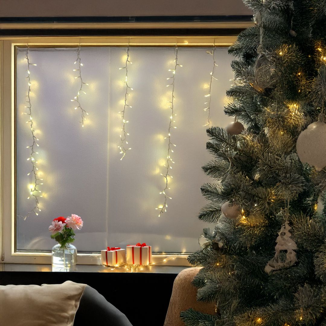 Tenda cluster con LED bianco caldo e fili che scendono di diverse lunghezze su una finestra con allestimento natalizio.