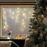 Tenda cluster con LED bianco caldo e fili che scendono di diverse lunghezze su una finestra con allestimento natalizio.