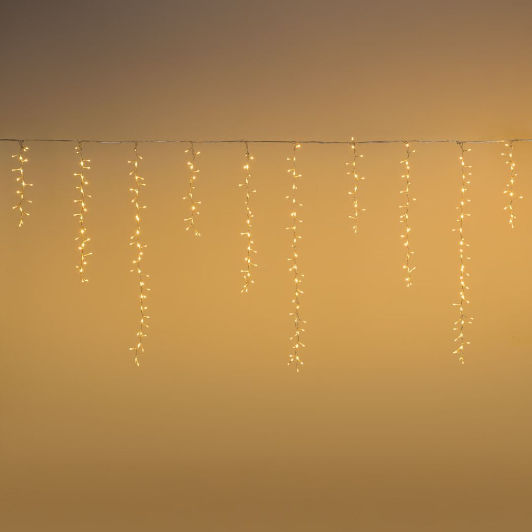 Tenda cluster con LED bianco caldo e fili che scendono di diverse lunghezze su sfondo oro.