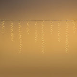 Tenda cluster con LED bianco caldo e fili che scendono di diverse lunghezze su sfondo oro.