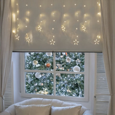 Tenda luminosa con stelle bianco caldo ambientate in un interno con finestra e divano.