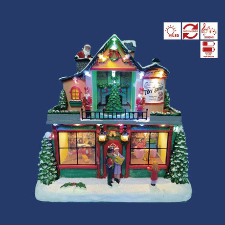 Negozio di giocattoli natalizio in miniatura con vetrine illuminate, albero di Natale, figure di persone sulla neve e Babbo Natale sul tetto su sfondo blu.