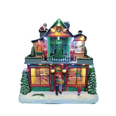 Negozio di giocattoli natalizio in miniatura con vetrine illuminate, albero di Natale, figure di persone sulla neve e Babbo Natale sul tetto su fondo bianco.