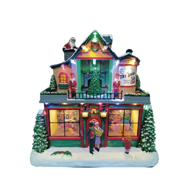 Negozio di giocattoli natalizio in miniatura con vetrine illuminate, albero di Natale, figure di persone sulla neve e Babbo Natale sul tetto su fondo bianco.