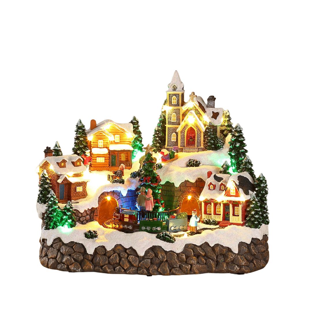 Villaggio natalizio in miniatura con case e chiesa illuminate, albero decorato al centro, trenino che passa in galleria e figure sulla neve.