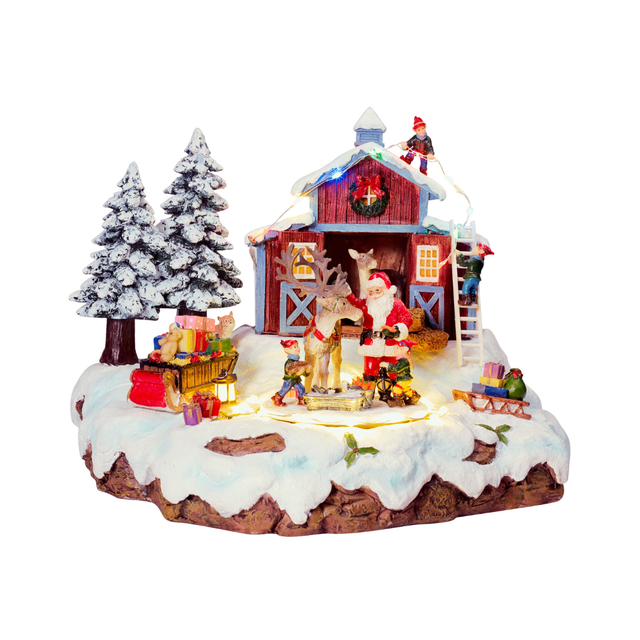 Villaggio natalizio innevato con Babbo Natale accanto a una renna davanti a una stalla rossa, elfi, regali, slitta, animali e alberi innevati, illuminato da luci LED
