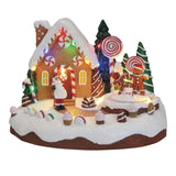 Casetta natalizia a tema gingerbread con luci colorate, decorazioni a caramella e personaggi a forma di biscotto nello scenario innevato.