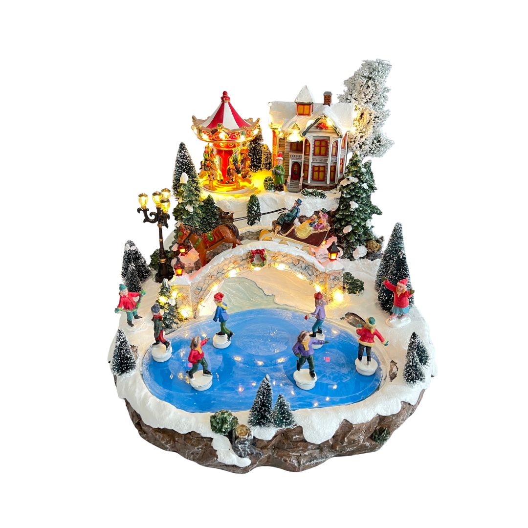 Villaggio natalizio in miniatura con pattinatori su lago ghiacciato, ponte illuminato, giostra a cavalli e casa decorata tra alberi innevati.