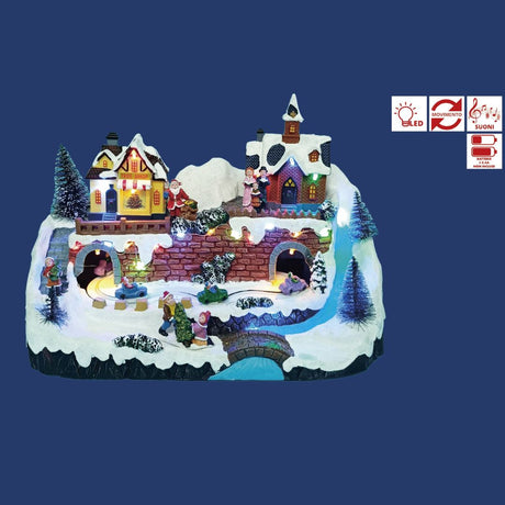 Villaggio natalizio in miniatura con negozio di alberi, chiesa illuminata, Babbo Natale, trenino che passa sotto ponti e figure di persone sulla neve su sfondo blu.