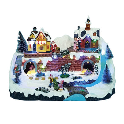 Villaggio natalizio in miniatura con negozio di alberi, chiesa illuminata, Babbo Natale, trenino che passa sotto ponti e figure di persone sulla neve.