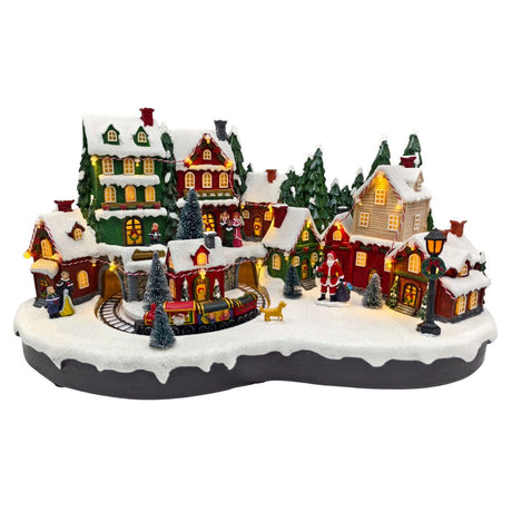 Villaggio natalizio in miniatura con case illuminate, trenino che attraversa gallerie, figure di persone e Babbo Natale sulla neve.